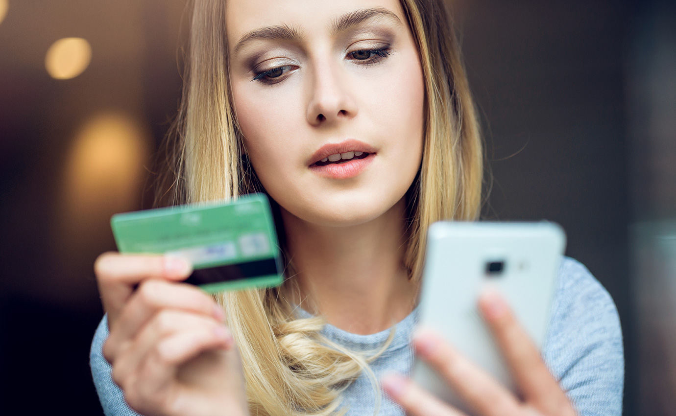 blonde woman looking at her green credit card and white cell phone