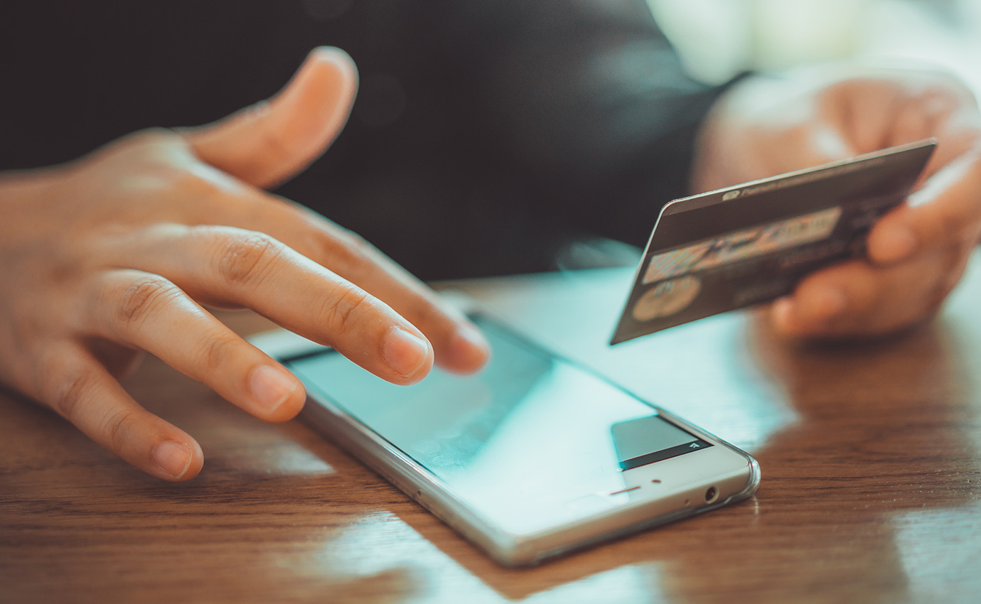 smart phone on wood desk below one hand holding grey credit card