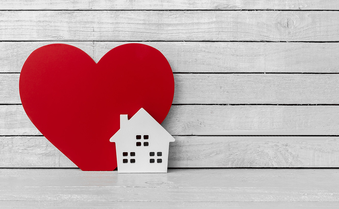 Small paper house in front of big, red paper heart