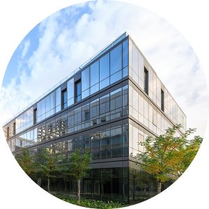 Heavily windowed office building with short trees against cloudy blue sky