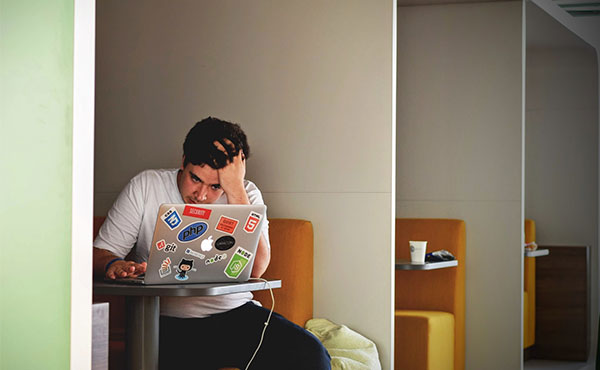 Disgruntled student sitting in cubby using silver laptop