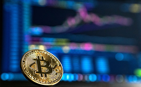 Gold bitcoin in front of blurred blue computer screens