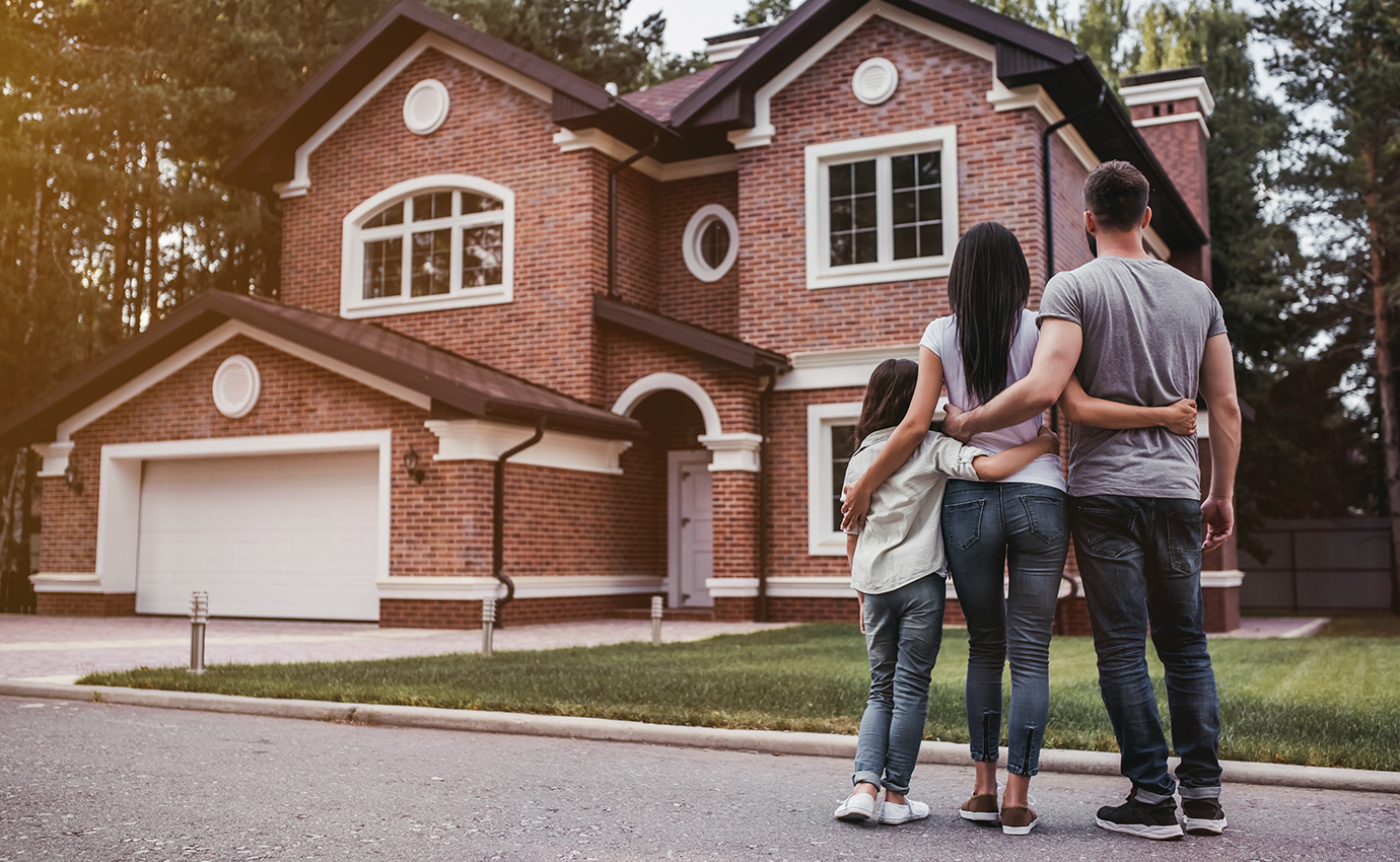 family of three standing in front of large red-brick house