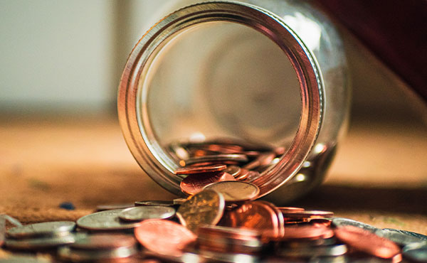 Glass jar of coins spilling coins on table