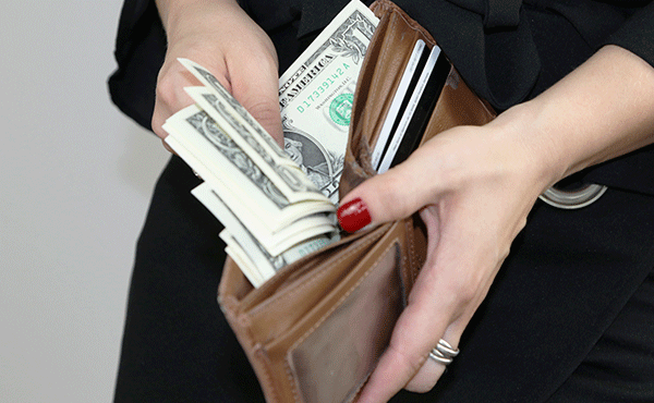 Image of woman's hands holding a tan, leather wallet and sorting through U.S. dollar bills.
