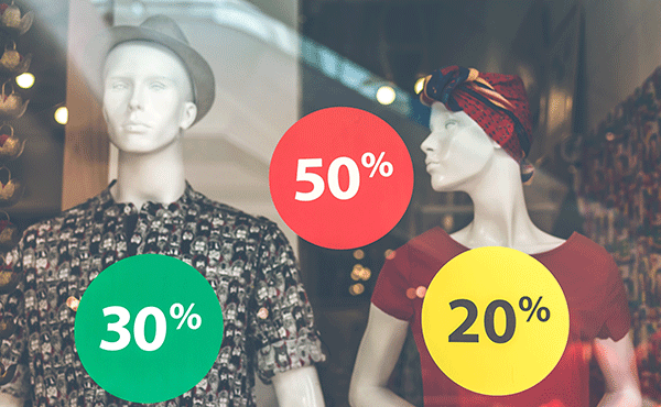 Two mannequins in shop window with green 20%, red 50%, and yellow 20% sale stickers.