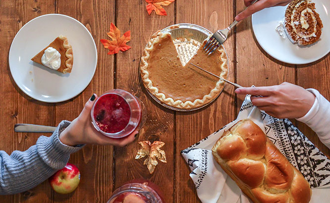 Image of people slicing pie and passing wine on a Thanksgiving table with various dishes.