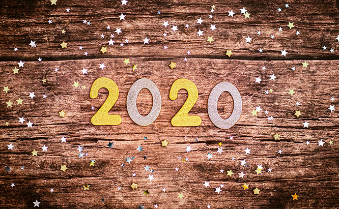 Silver and gold colored New Year's "2020" numbers on wooden surface with silver and gold stars scattered around.