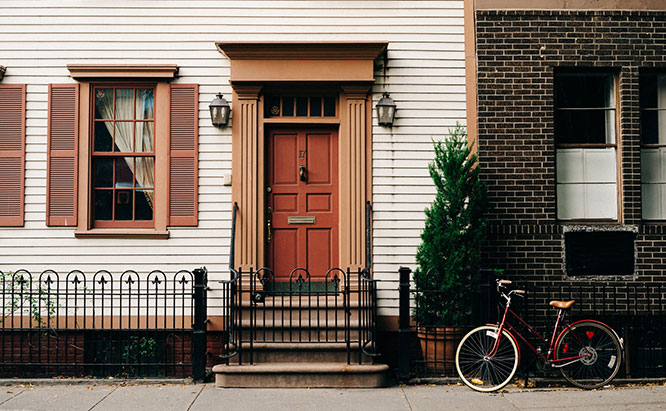 Image of home with peach colored shutters and burnt orange door next to dark brick building