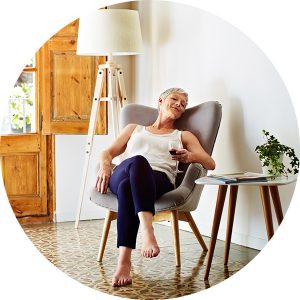 Reverse-Mortgage Older barefoot woman in a grey lounge chair holding glass of red wine.